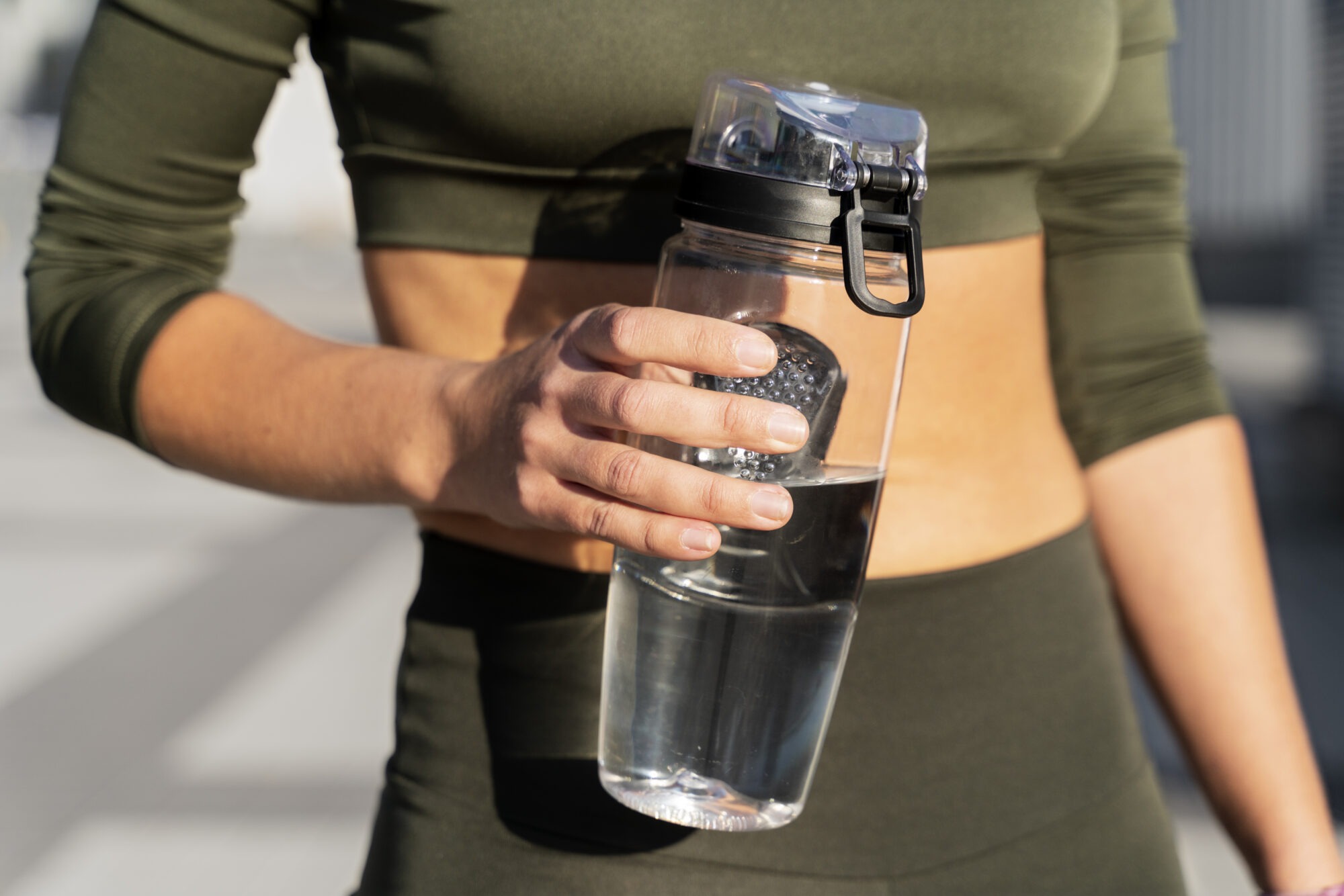 Focus sur une gourde transparente tenue par une femme en tenue de sport